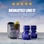Two bottles of Sip Elixirs with a glass of liquid and garnish on a wooden surface with a blue sky background.